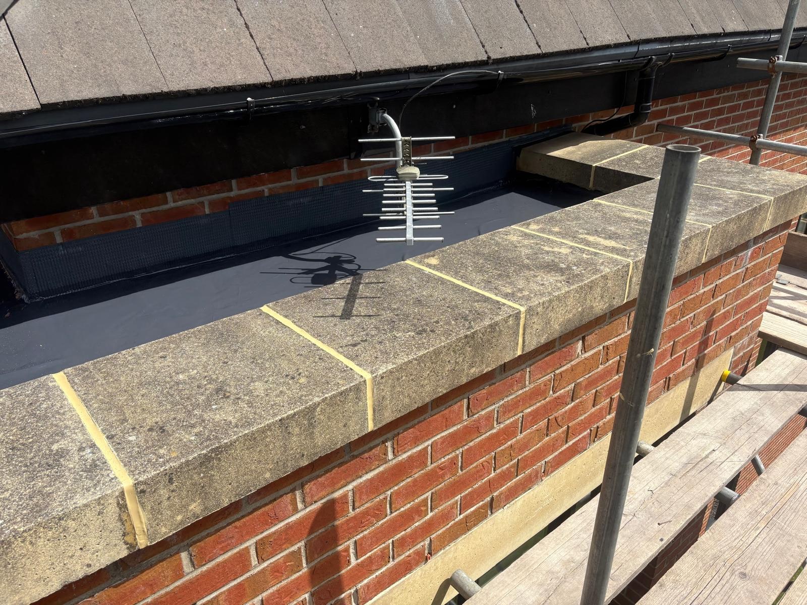 A dark flat roof membrane behind a stone coped brick parapet