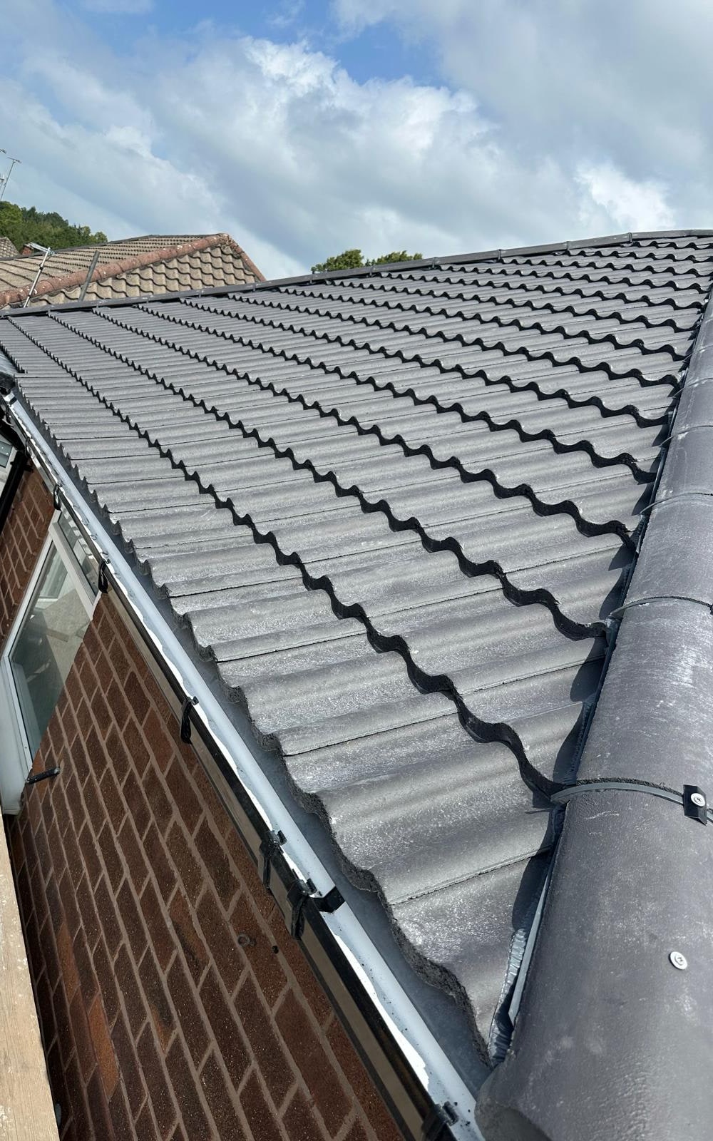 A finished grey tiled roof with a bedded ridge and new black gutter